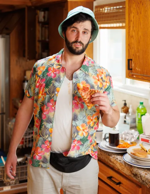 A comedian in a loud shirt and bucket hat in a kitchen