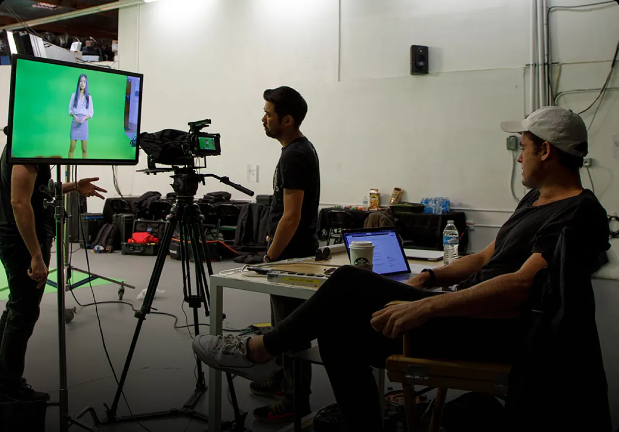 A green-screen studio with the crew at the edit desk