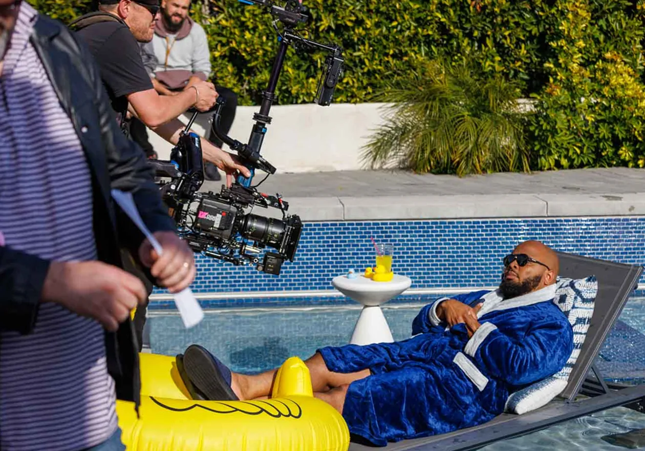 A crew filming a comedian in a bathrobe by a pool