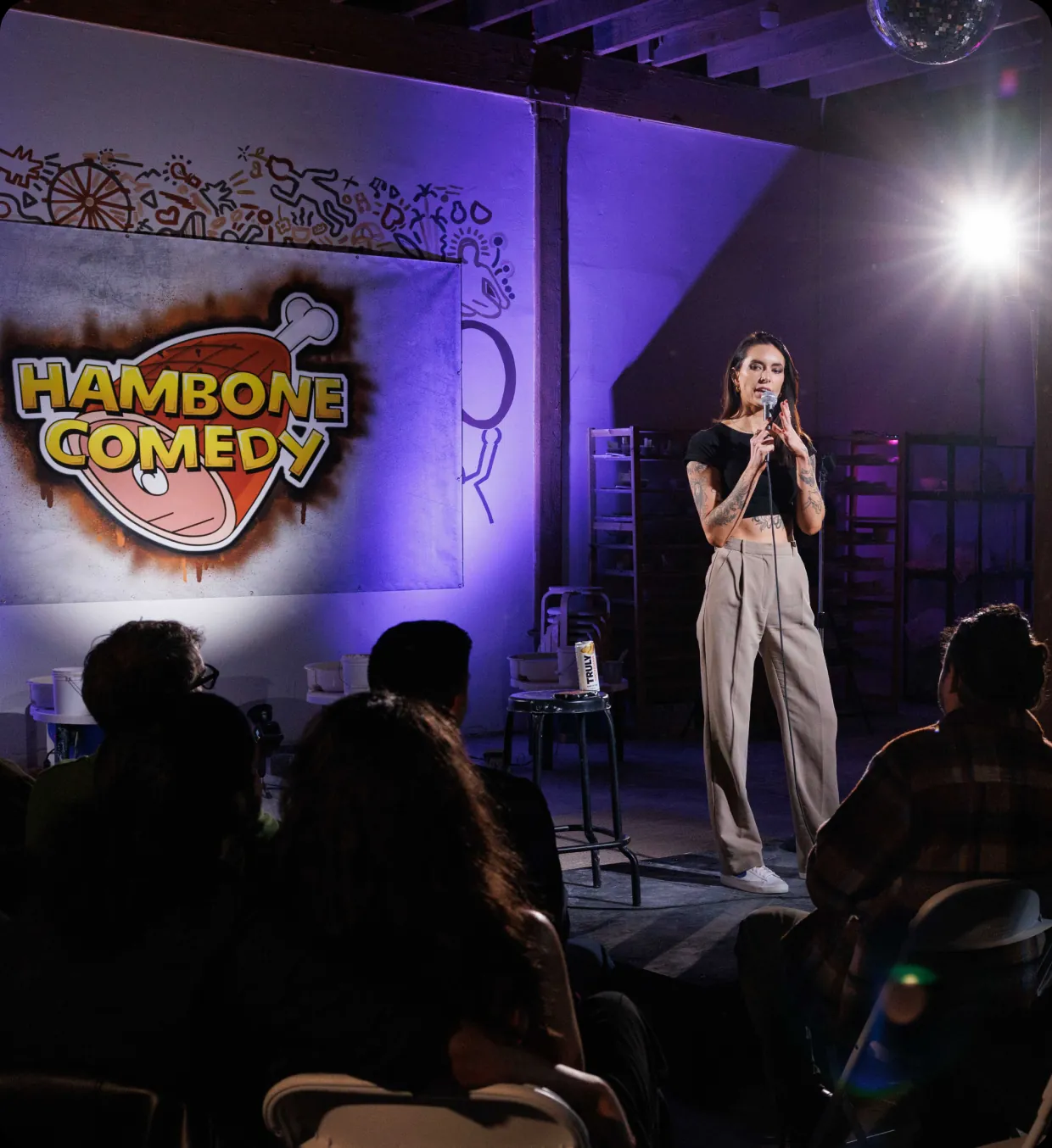 A comedian on stage in front of the Hambone Comedy backdrop